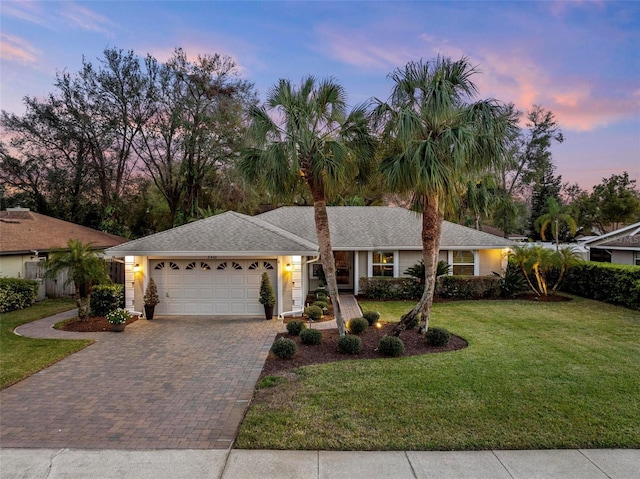 ranch-style home featuring a garage, a front yard, decorative driveway, and stucco siding