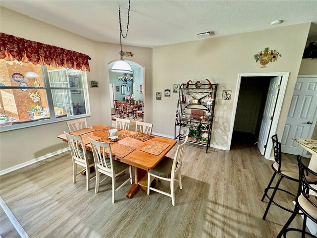 dining area with wood finished floors, visible vents, baseboards, arched walkways, and a textured ceiling