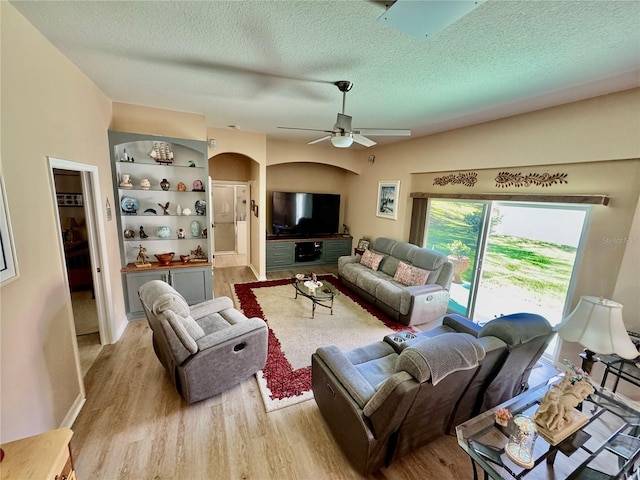 living area with light wood-type flooring, arched walkways, a textured ceiling, and ceiling fan