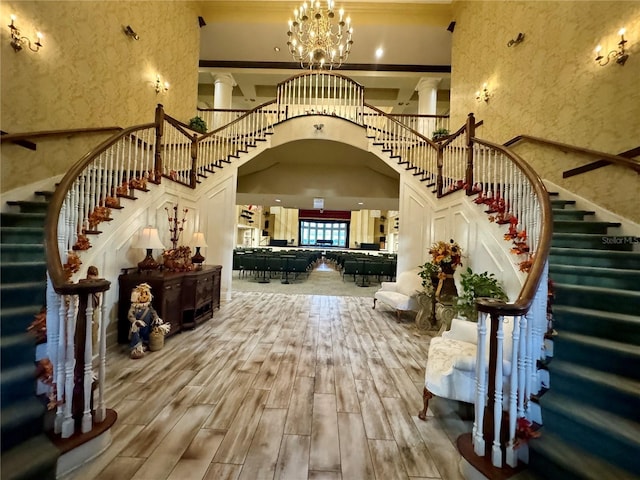 entryway featuring wood finish floors, a towering ceiling, stairs, and ornate columns