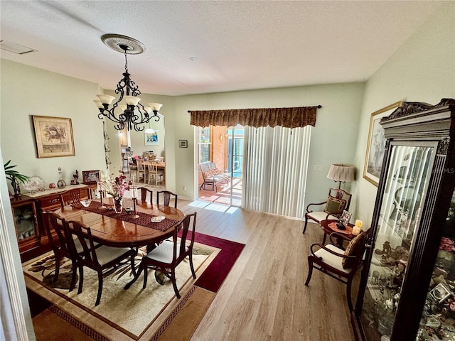 dining room with visible vents, a notable chandelier, wood finished floors, and a textured ceiling