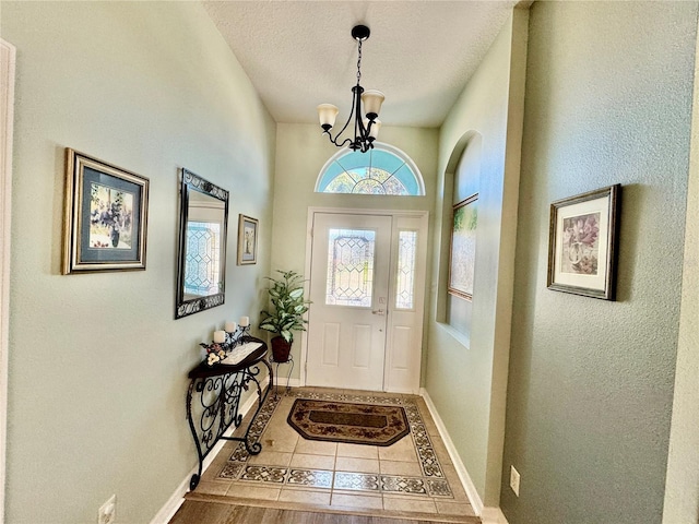 tiled foyer with baseboards, a chandelier, and a textured ceiling