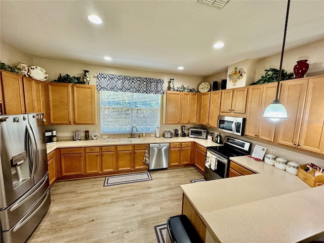 kitchen featuring a sink, decorative light fixtures, stainless steel appliances, light wood-style floors, and light countertops