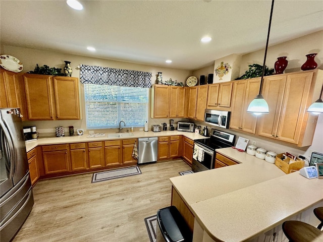 kitchen featuring light wood-style flooring, a sink, light countertops, appliances with stainless steel finishes, and a kitchen bar