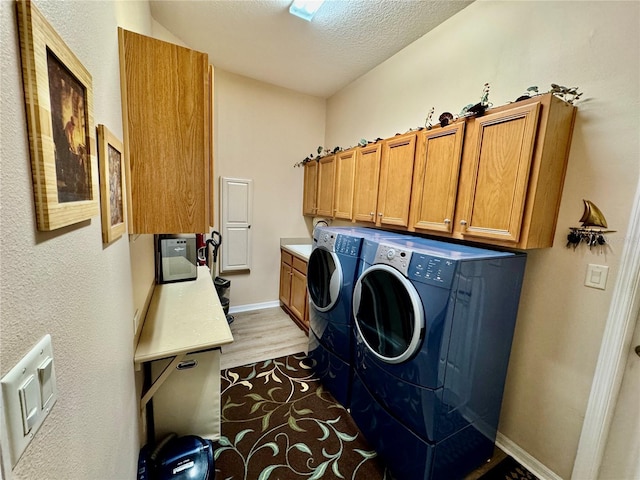 laundry room featuring washer and dryer, a textured ceiling, cabinet space, light wood finished floors, and baseboards