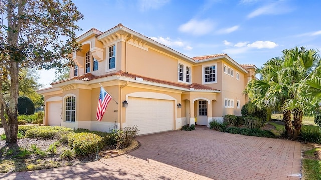 mediterranean / spanish-style house featuring a tiled roof, decorative driveway, an attached garage, and stucco siding