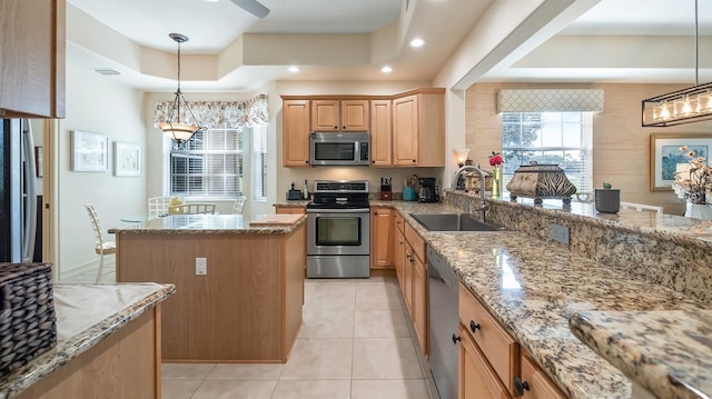 kitchen with a raised ceiling, a center island, light stone countertops, stainless steel appliances, and a sink