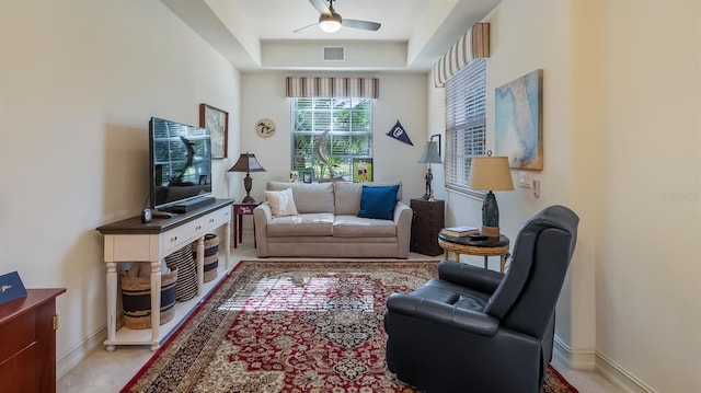 living area featuring baseboards, a tray ceiling, visible vents, and a ceiling fan