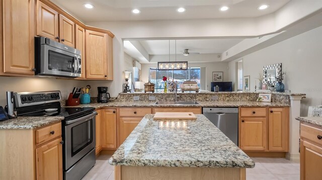 kitchen with a center island, stainless steel appliances, a sink, light stone countertops, and a peninsula