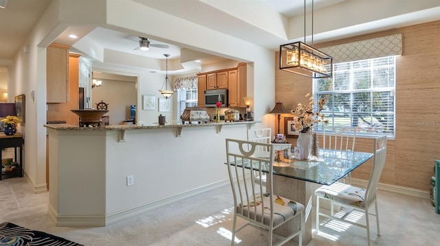 kitchen with stone counters, wooden walls, stainless steel microwave, and a raised ceiling