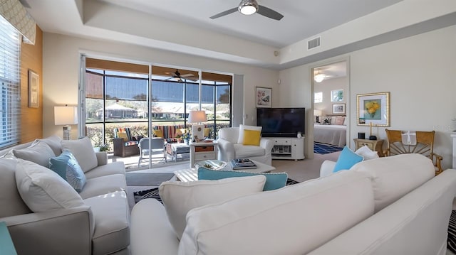 living area with visible vents, a raised ceiling, and a ceiling fan