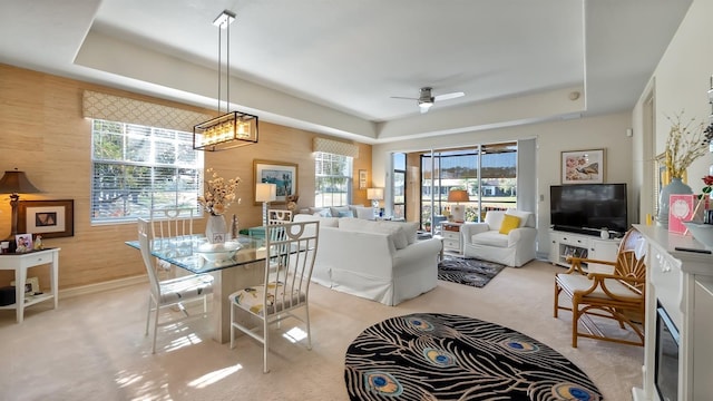 dining space featuring a raised ceiling, light carpet, ceiling fan, and wooden walls