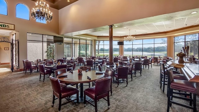 carpeted dining space with a high ceiling, baseboards, a tray ceiling, decorative columns, and an inviting chandelier