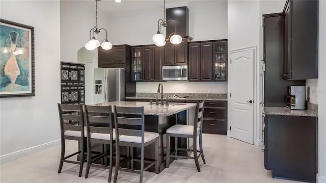 kitchen featuring a breakfast bar area, a high ceiling, appliances with stainless steel finishes, glass insert cabinets, and dark brown cabinetry