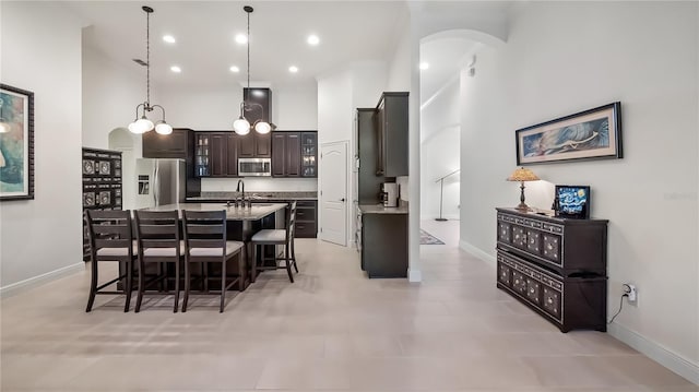 kitchen featuring dark brown cabinetry, a high ceiling, appliances with stainless steel finishes, an island with sink, and a kitchen bar