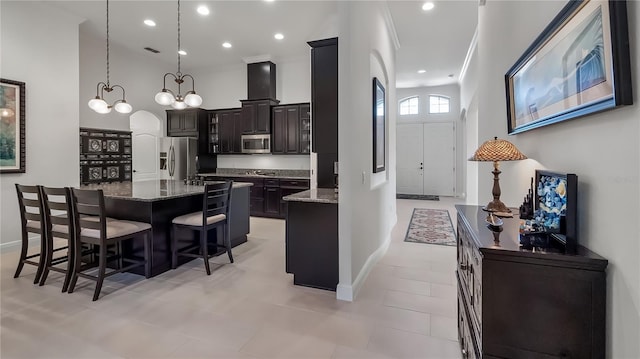 kitchen featuring stainless steel appliances, a center island, a towering ceiling, and light stone countertops