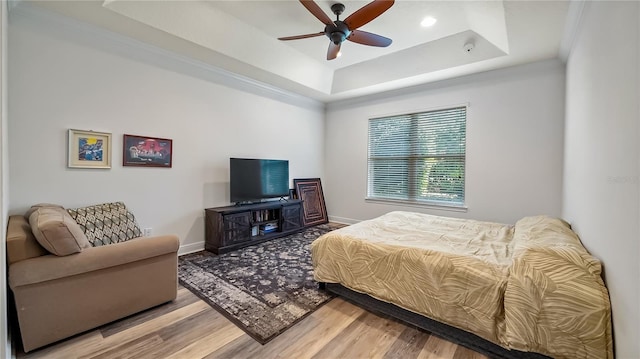 bedroom featuring light wood-style floors, a raised ceiling, ceiling fan, and baseboards