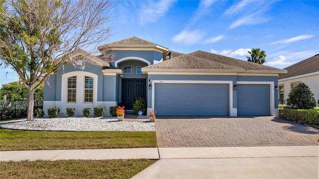 view of front of property with decorative driveway, fence, an attached garage, and stucco siding