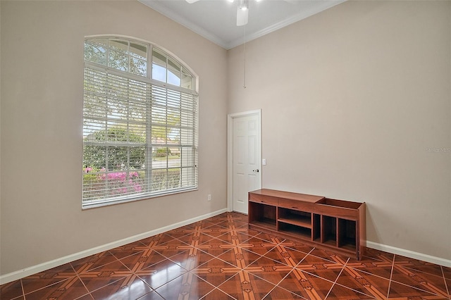 unfurnished room with a high ceiling, crown molding, baseboards, and ceiling fan