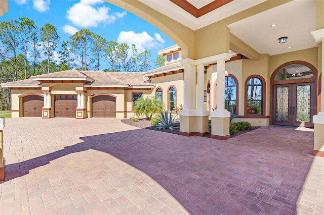 view of front of house with a tiled roof, stucco siding, french doors, decorative driveway, and a garage