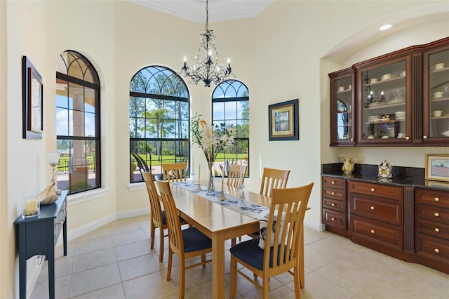 dining space with a notable chandelier, a high ceiling, crown molding, light tile patterned floors, and baseboards