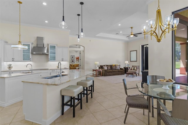 kitchen featuring wall chimney range hood, ornamental molding, a center island with sink, and a sink