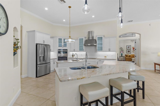 kitchen featuring arched walkways, ornamental molding, a large island, appliances with stainless steel finishes, and wall chimney exhaust hood