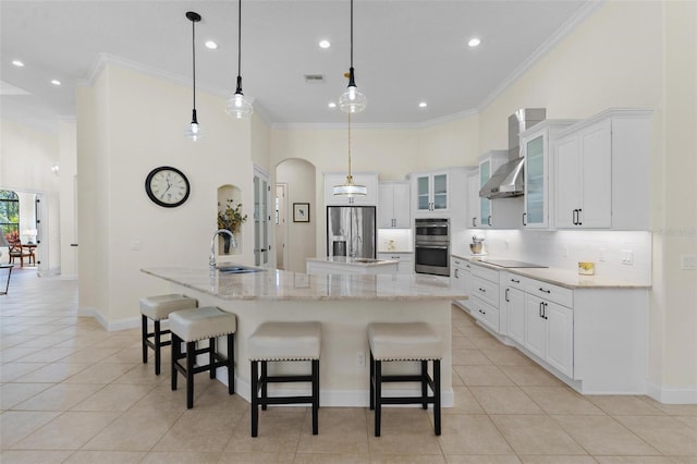 kitchen featuring a sink, a spacious island, arched walkways, appliances with stainless steel finishes, and wall chimney exhaust hood