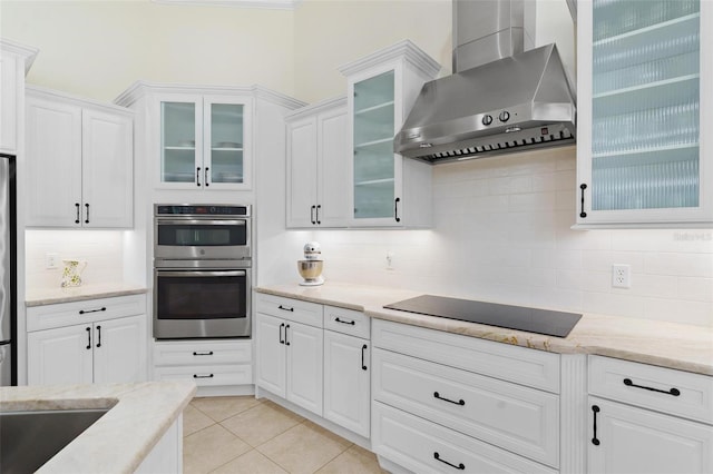 kitchen with light tile patterned floors, stainless steel appliances, white cabinets, wall chimney exhaust hood, and tasteful backsplash