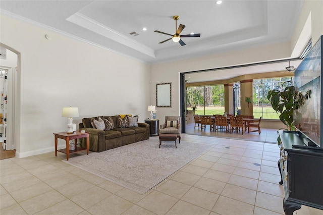 living area with a tray ceiling, light tile patterned floors, crown molding, and ceiling fan