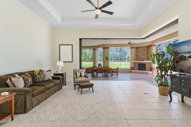 living room featuring a stone fireplace, crown molding, tile patterned flooring, a raised ceiling, and ceiling fan