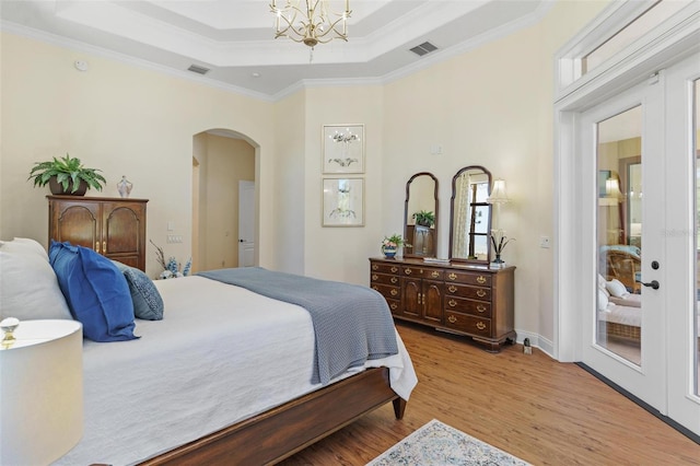 bedroom with wood finished floors, visible vents, arched walkways, crown molding, and a raised ceiling