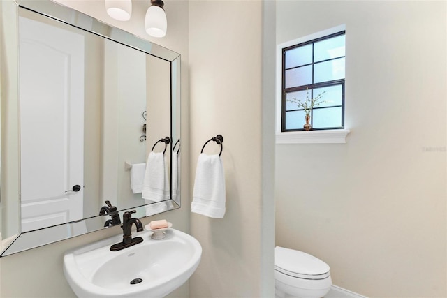 half bathroom featuring toilet, baseboards, and a sink