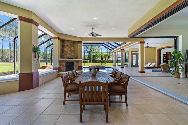 view of patio with glass enclosure, outdoor dining area, an outdoor stone fireplace, and a ceiling fan