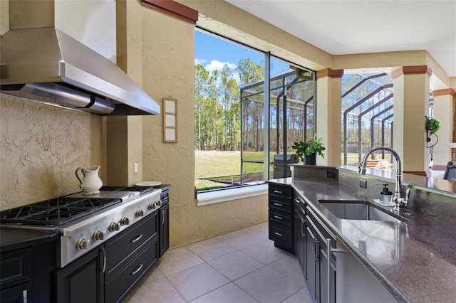 kitchen featuring a textured wall, range hood, dark cabinetry, stainless steel gas stovetop, and a sink