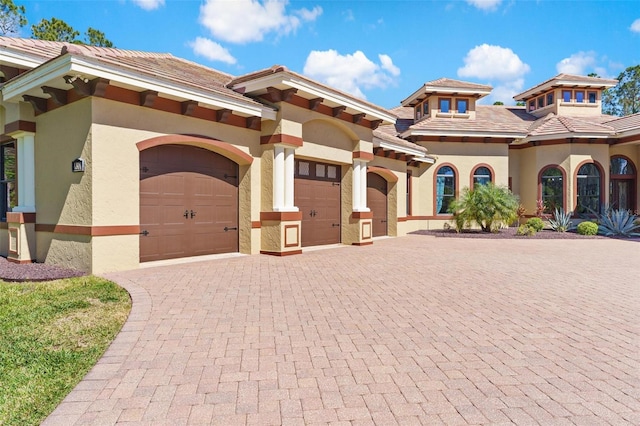 mediterranean / spanish-style house with a tiled roof, decorative driveway, an attached garage, and stucco siding