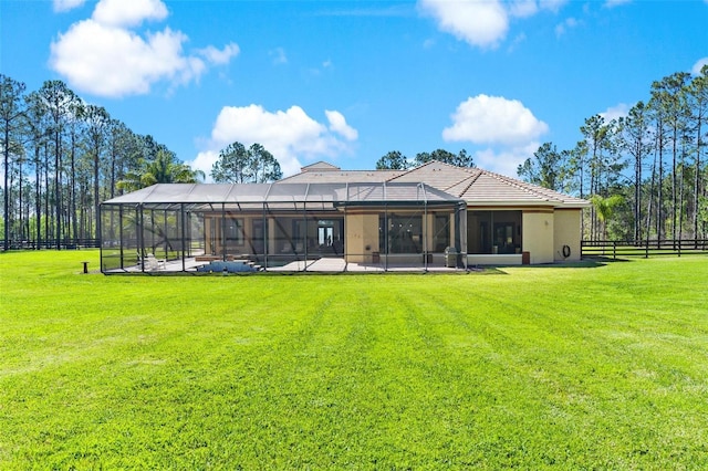 rear view of house featuring a lawn, glass enclosure, and fence