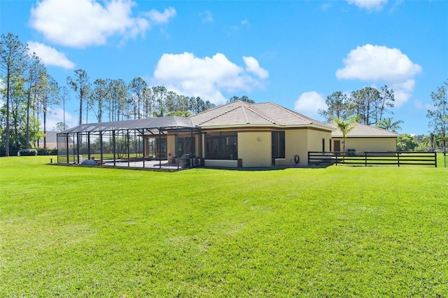 rear view of property featuring stucco siding, glass enclosure, a lawn, and fence