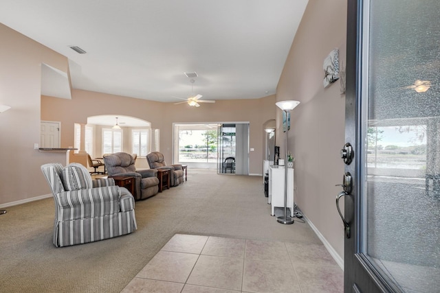 carpeted living area featuring arched walkways, ceiling fan, visible vents, baseboards, and tile patterned floors