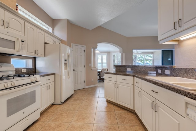 kitchen featuring arched walkways, light tile patterned flooring, white appliances, a sink, and dark countertops