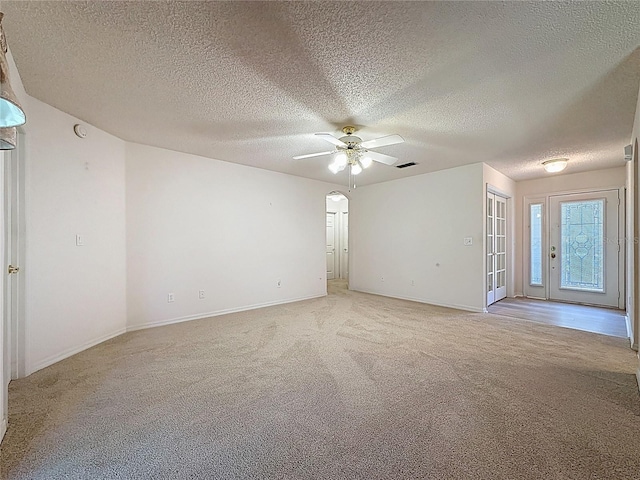 unfurnished room with ceiling fan, arched walkways, baseboards, and light colored carpet