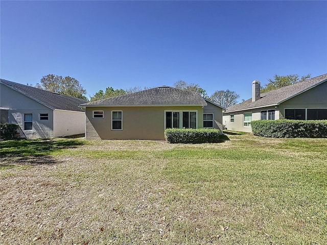 rear view of property featuring a lawn and stucco siding