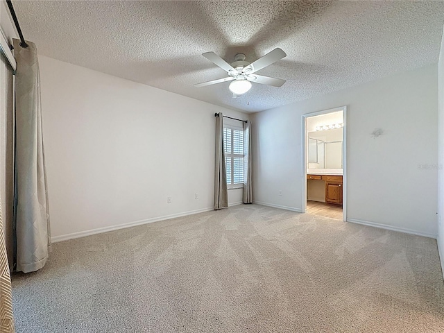 unfurnished bedroom with light colored carpet, connected bathroom, ceiling fan, a textured ceiling, and baseboards