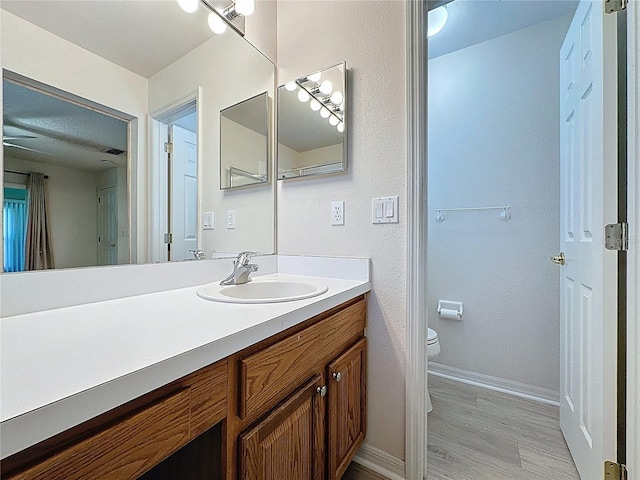 bathroom with wood finished floors, vanity, toilet, and baseboards