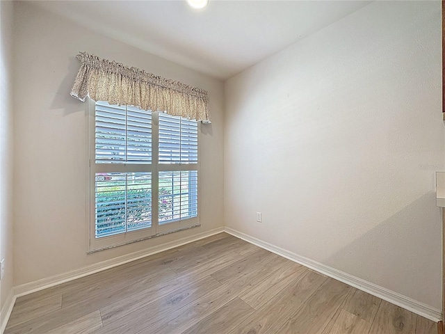 spare room with baseboards and wood finished floors