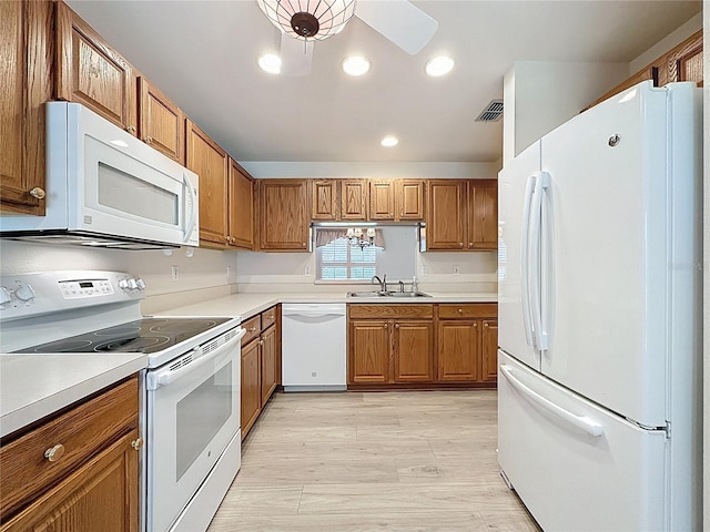 kitchen with white appliances, brown cabinetry, a sink, and light wood-style floors