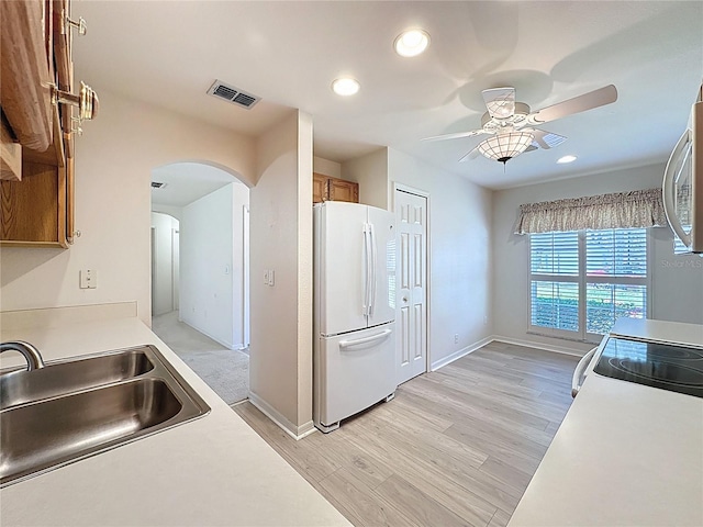 kitchen featuring arched walkways, white appliances, a sink, visible vents, and brown cabinets