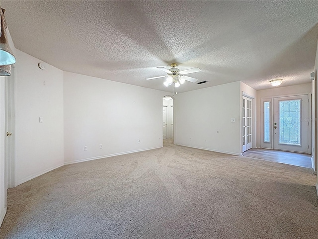 unfurnished room featuring a ceiling fan, arched walkways, light colored carpet, and baseboards