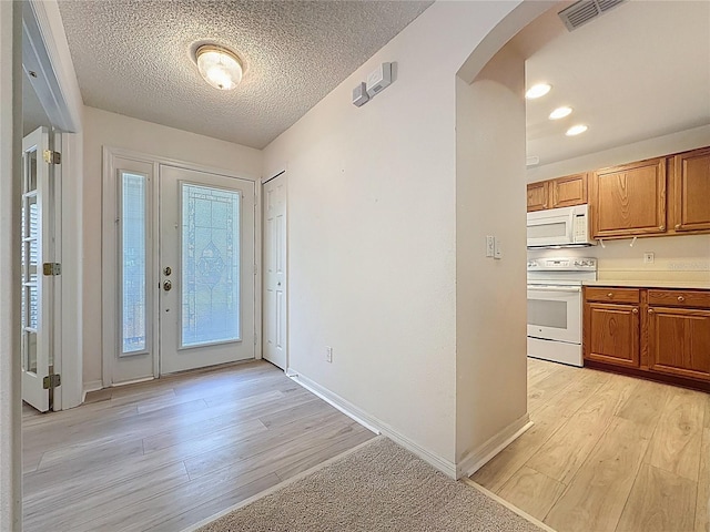 foyer entrance featuring arched walkways, a textured ceiling, visible vents, baseboards, and light wood-type flooring