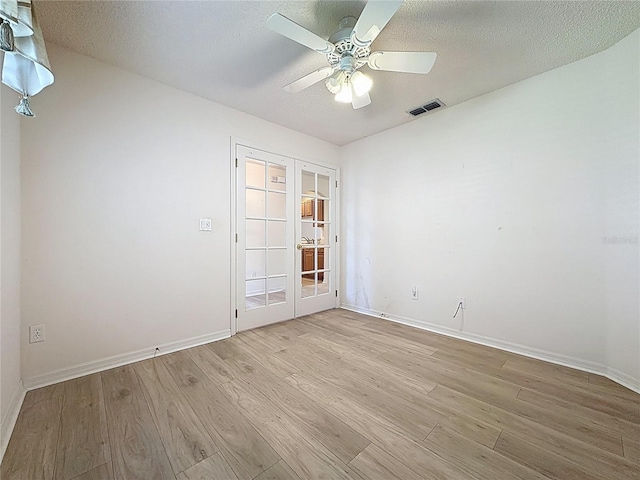 empty room featuring light wood-style floors, visible vents, a textured ceiling, and french doors